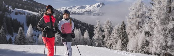 Twee skiërs in kleurrijke kleding op besneeuwde piste met bergen op de achtergrond