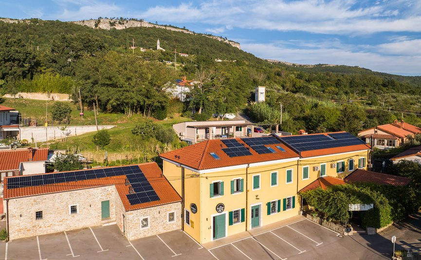 Building with solar panels on roof near wooded hill