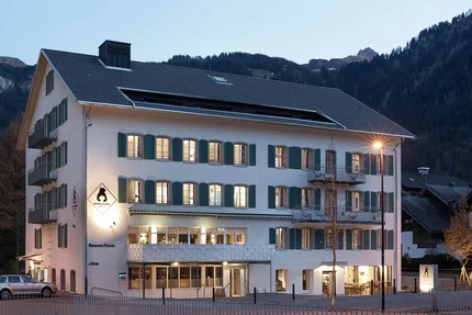 Verlicht hotelgebouw met bergen op de achtergrond bij schemering