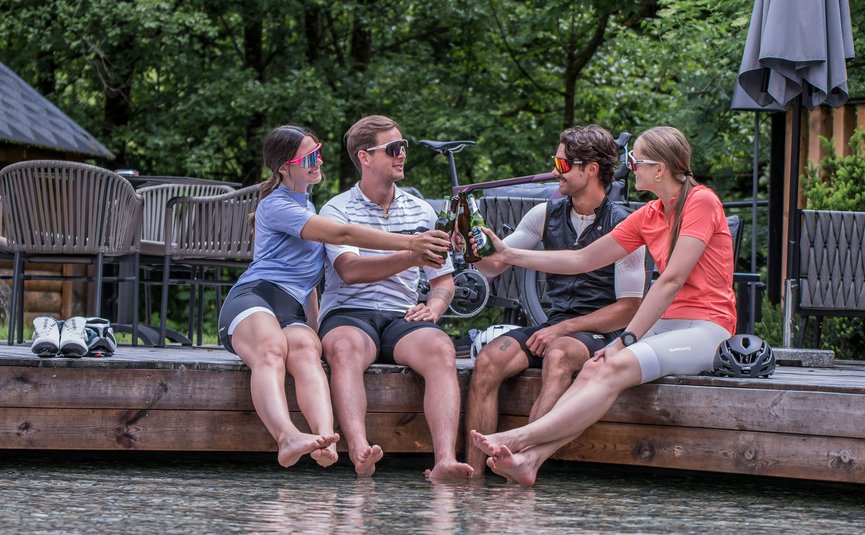 Vier fietsers proosten met flessen terwijl ze aan het water zitten