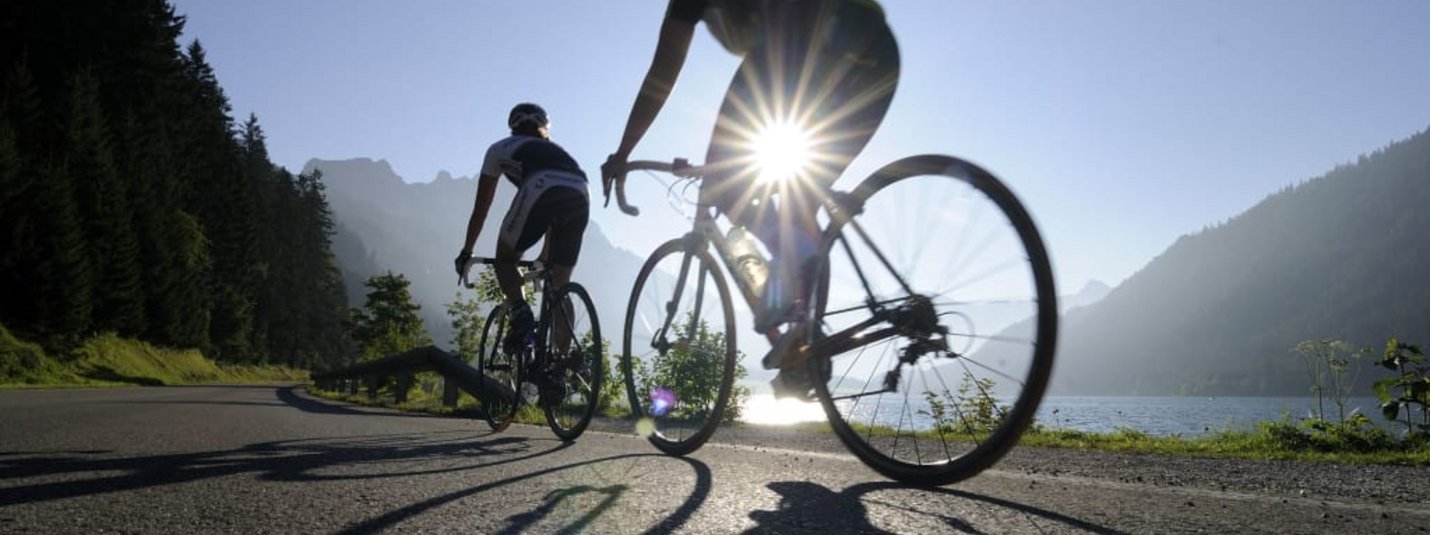 Due ciclisti su strada di montagna vicino a un lago al sole