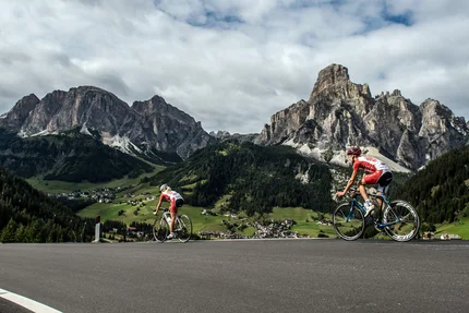Due ciclisti salgono in salita nelle Dolomiti con villaggio nella valle