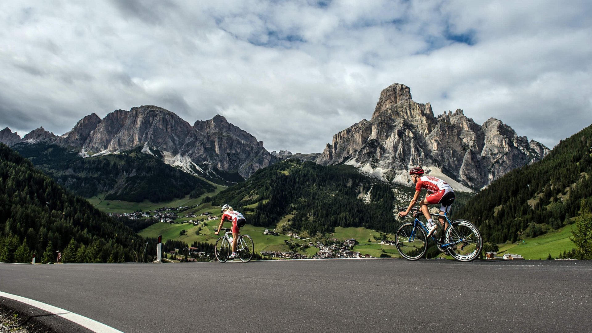 Zwei Radfahrer fahren bergauf in den Dolomiten mit Dorf im Tal