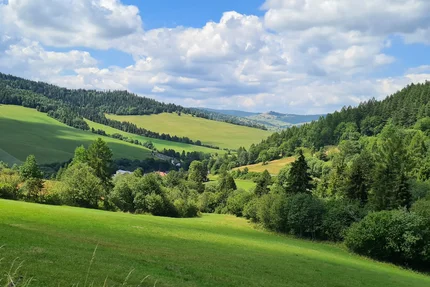 View of green hills and forests under blue sky with clouds