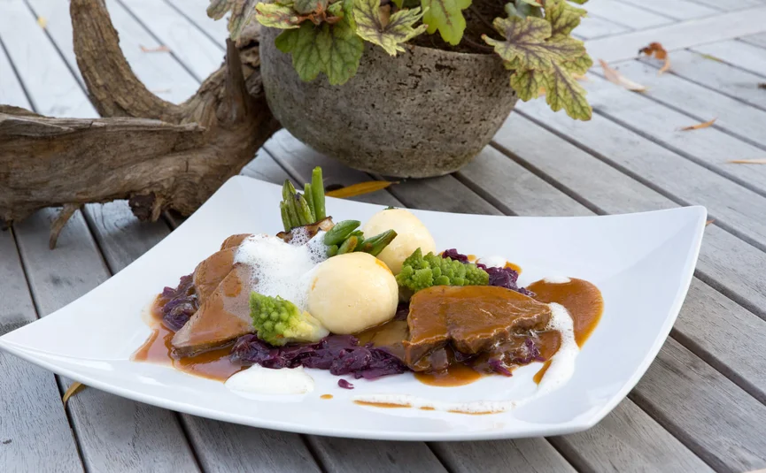 Piatto elegante con carne, canederli e verdure su piatto bianco