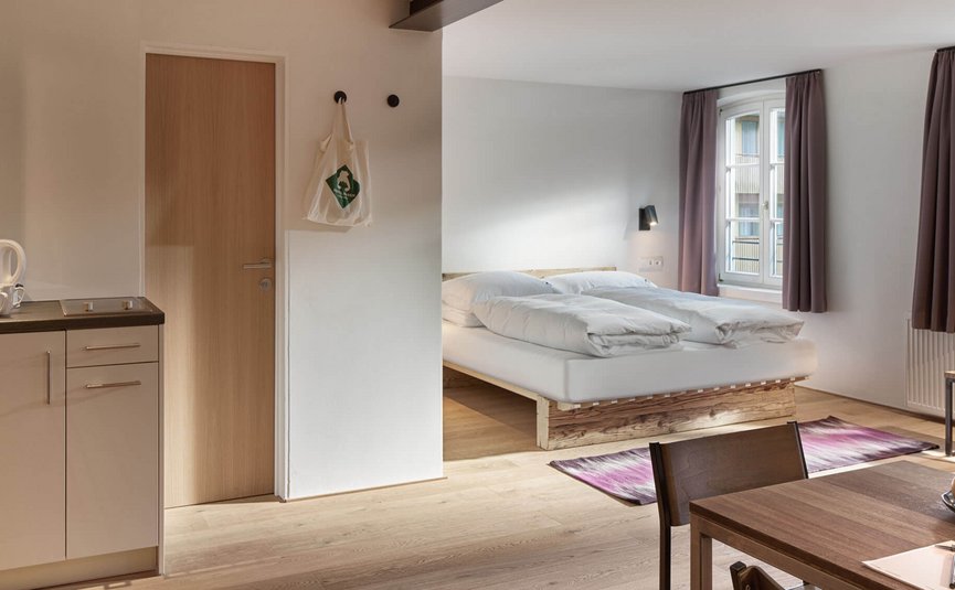 Bright room with kitchenette, dining table, and double bed by windows