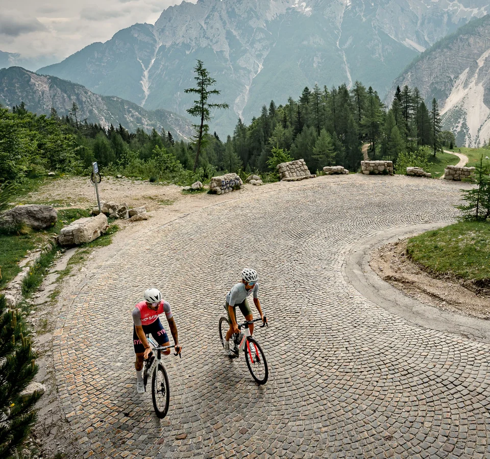 Zwei Radfahrer fahren eine kurvige Bergstraße mit steilen Felsen im Hintergrund