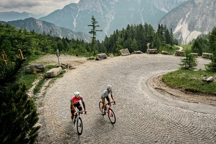 Twee wielrenners op een kronkelende bergweg met steile rotskliffen