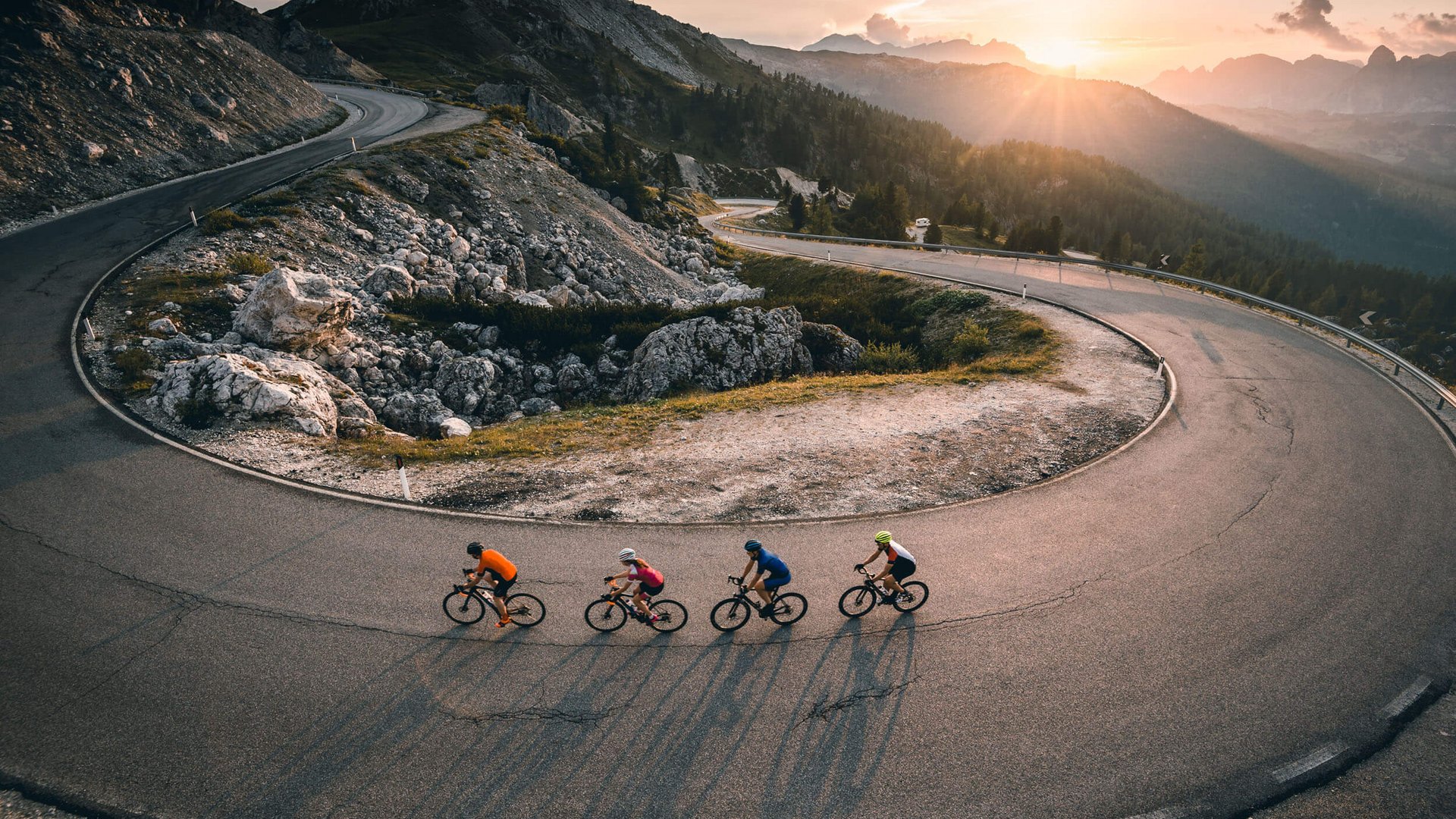 Four cyclists riding on a mountain road at sunset