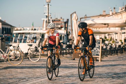 Two cyclists, man and woman, riding on a paved path by the water