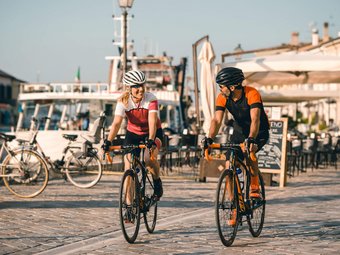 Zwei Radfahrer, Mann und Frau, fahren auf gepflastertem Weg am Wasser