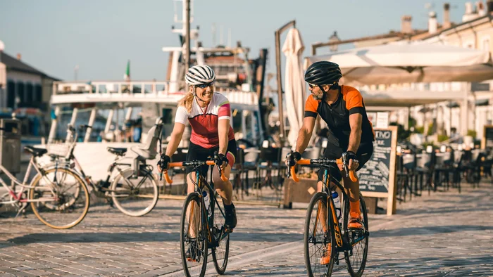 Two cyclists, man and woman, riding on a paved path by the water