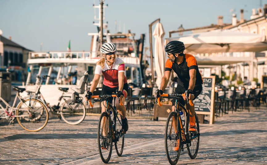 Two cyclists, man and woman, riding on a paved path by the water