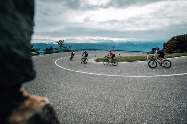 Hotels © Jens Scheibe Vier Radfahrer fahren eine kurvige Bergstraße bei bewölktem Himmel
