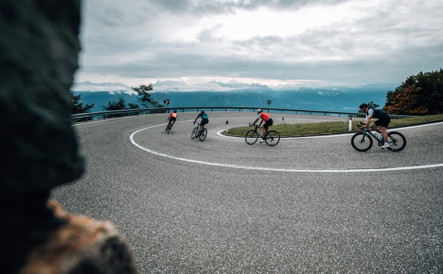 Quattro ciclisti su una strada di montagna tortuosa con cielo nuvoloso