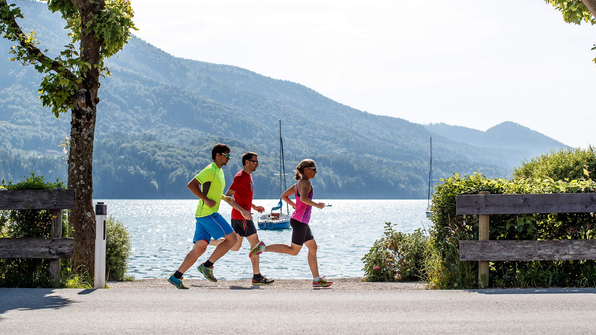 Triathlon Hotels: Deine Base für Training & Erholung © Erwin Haiden Drei Personen joggen am See mit Bergen im Hintergrund