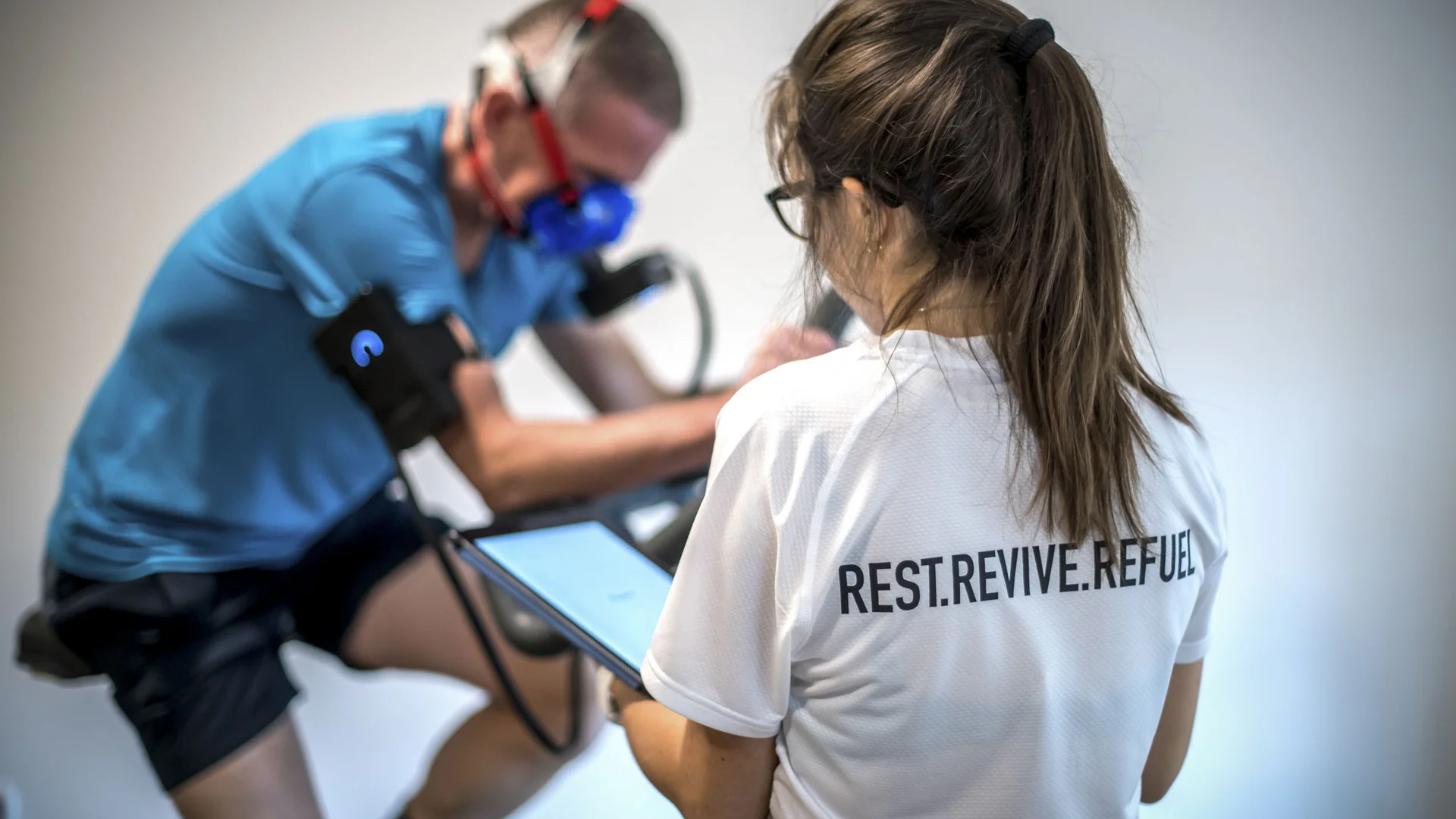 Frau überwacht Mann mit Atemmaske während Training auf Fahrrad-Ergometer