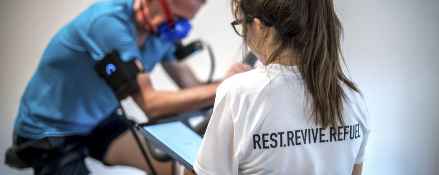 Vrouw die man met ademhalingsmasker monitort tijdens trainen op hometrainer