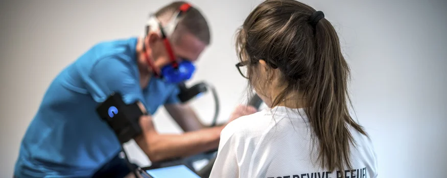 Frau überwacht Mann mit Atemmaske während Training auf Fahrrad-Ergometer