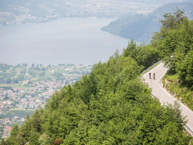 Die schönsten Rennrad-Regionen und Tipps für den Herbst © Heiko Mandl Zwei Radfahrer fahren bergauf auf kurviger Straße mit Seenblick