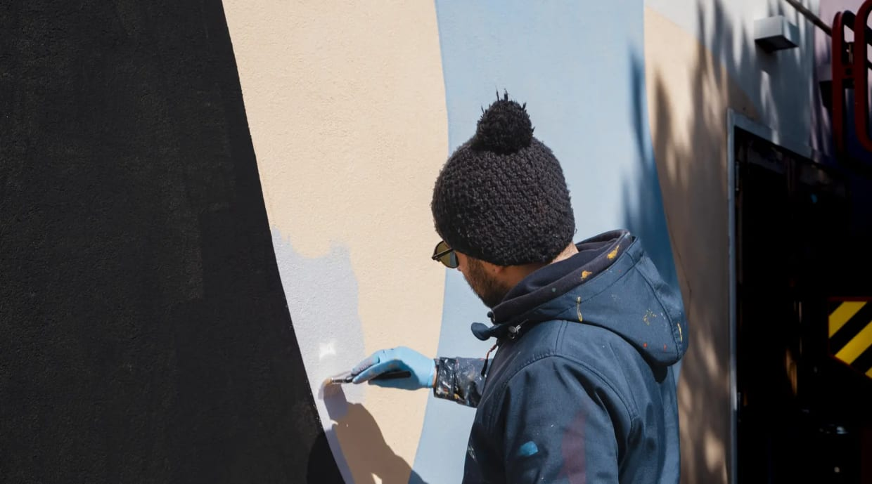 Frühling mit Ihrem vierbeinigen Freund Mann mit Mütze malt Wand mit Pinsel und blauer Farbe
