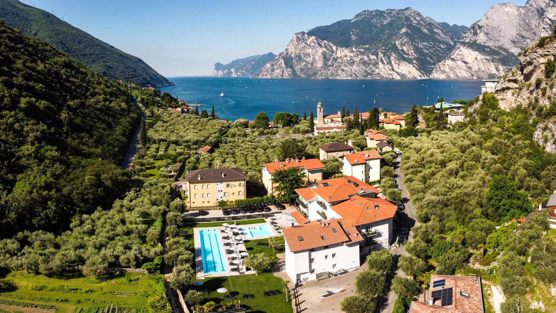 Dorf mit Swimmingpool am Seeufer umgeben von Bergen und Olivenhainen