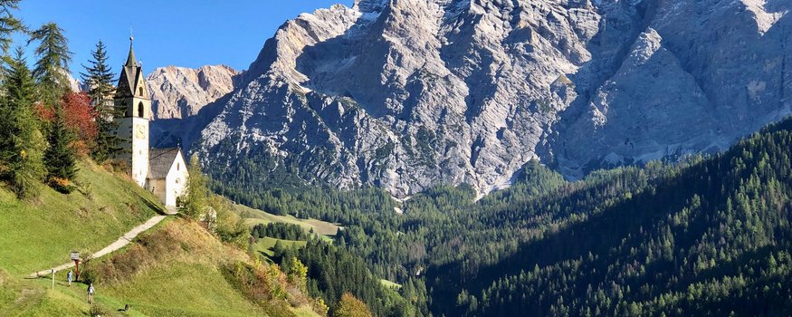 Hotel Ostaria Posta **** © Hotel Ostaria Posta Chiesa su una collina con montagna e bosco sullo sfondo sotto cielo limpido