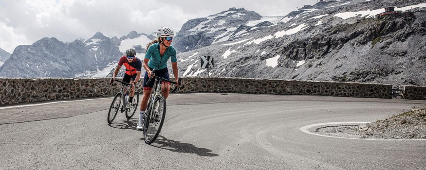 Alpen-Comfort-Hotel Central **** © Felix Saller Zwei Radfahrer fahren eine Bergstraße mit schneebedeckten Gipfeln im Hintergrund