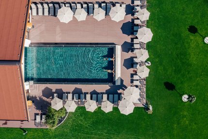 Menschen schwimmen in einem Pool mit Liegestühlen und Sonnenschirmen bei einem grünen Rasen