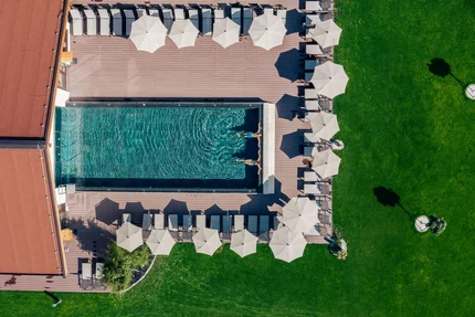 People swimming in a pool surrounded by lounge chairs and umbrellas on green grass