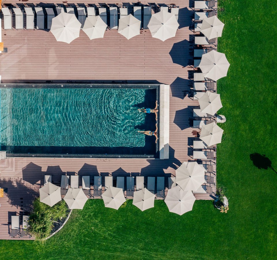 Menschen schwimmen in einem Pool mit Liegestühlen und Sonnenschirmen bei einem grünen Rasen