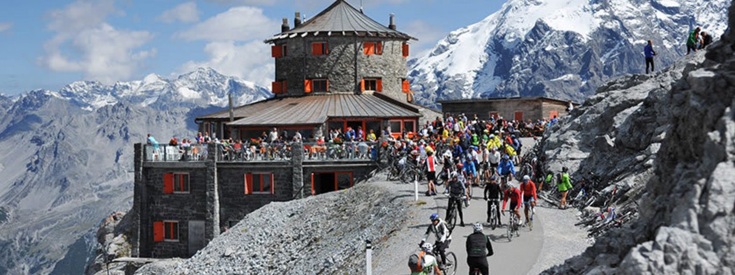Radfahrer fahren auf Bergstraße zum Berghotel mit Menschen und schneebedecktem Berg