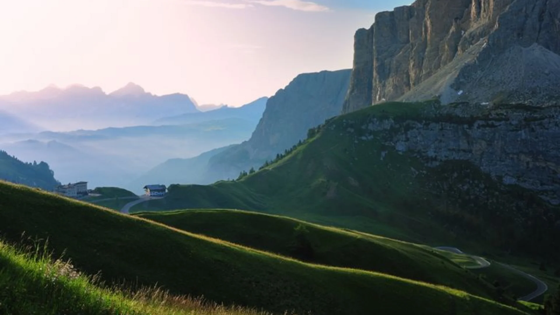 Green hills and mountain cliffs at sunrise in the Alps