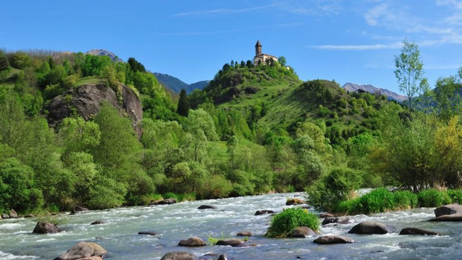 Ein Rennrad-Wochenende in Südtirols Süden © Hotel Teutschhaus Kurtinig Fluss mit Steinen vor einem Hügel mit Kapelle und bewaldeten Bergen