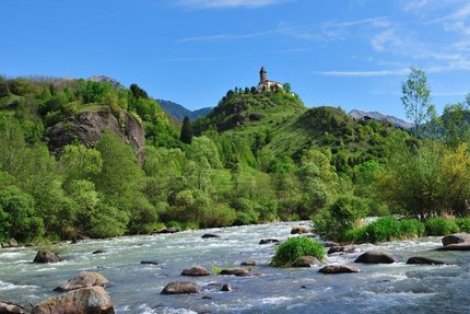 Rivier met stenen, heuvel met kapel en beboste bergen op de achtergrond