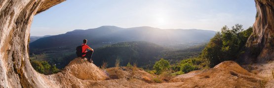 Persona seduta in una grotta che guarda il paesaggio montano soleggiato