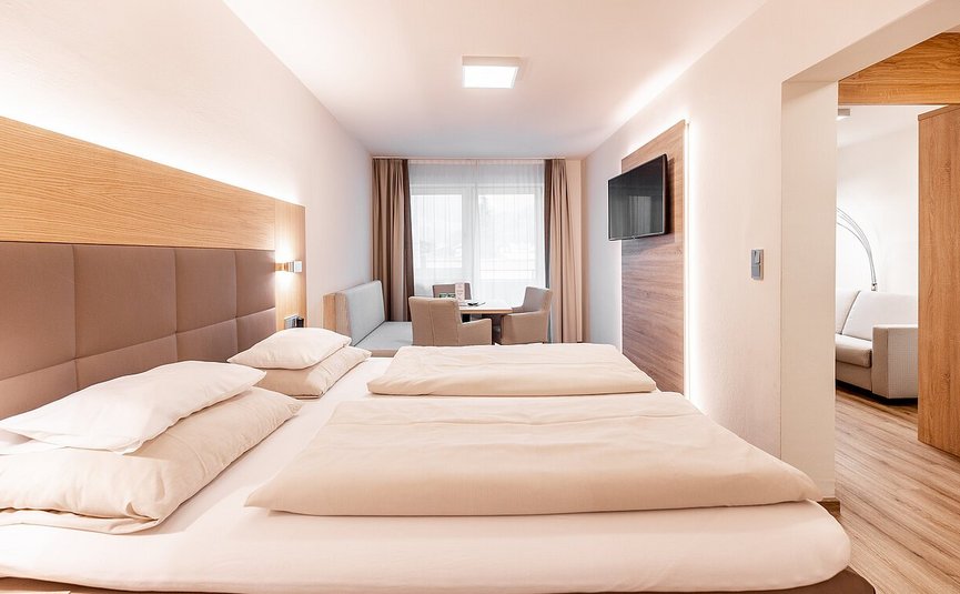Modern hotel room with double bed, seating area, and TV