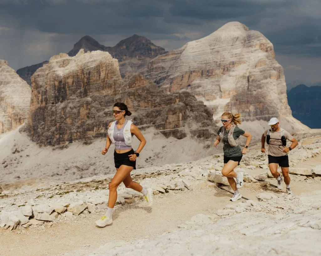 Three runners on a rocky mountain trail before impressive Dolomite peaks