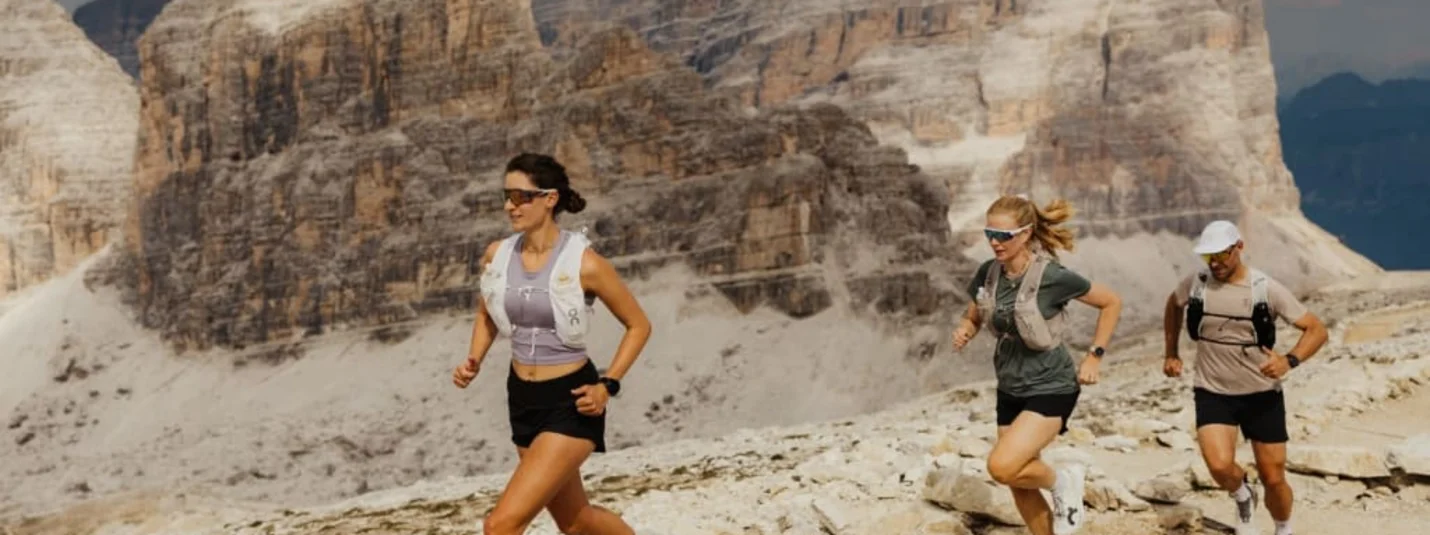 Salté – Trail running experience Tre corridori su un sentiero roccioso davanti alle imponenti Dolomiti
