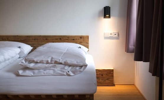 Gemachtes Bett mit weißer Bettwäsche und Nachtlampe an der Wand