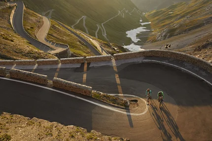 Zwei Radfahrer fahren eine kurvenreiche Bergstraße im Sonnenlicht hinauf