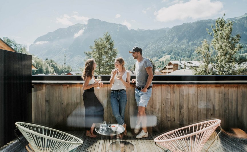 Three people chatting on a terrace with mountain views