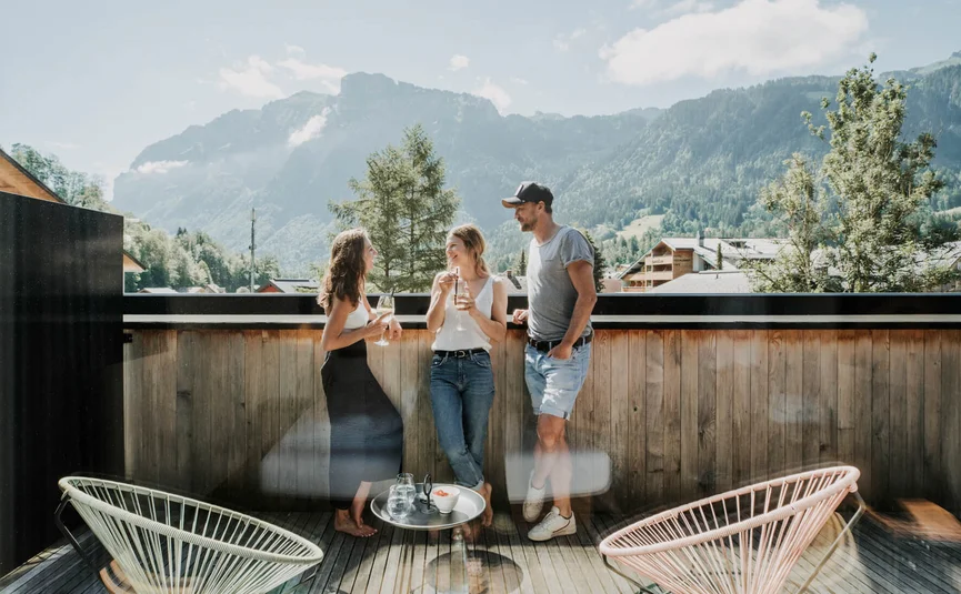 Drei Personen unterhalten sich auf einer Terrasse mit Bergblick