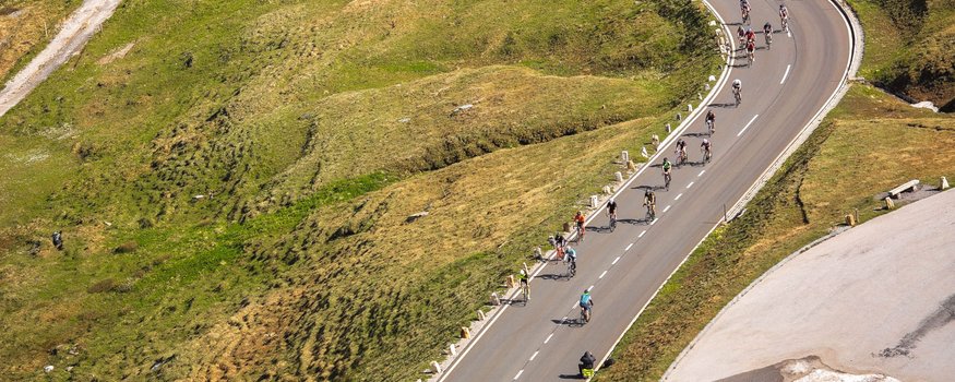 Ciclisti su strada di montagna tortuosa con erba verde e chiazze di neve