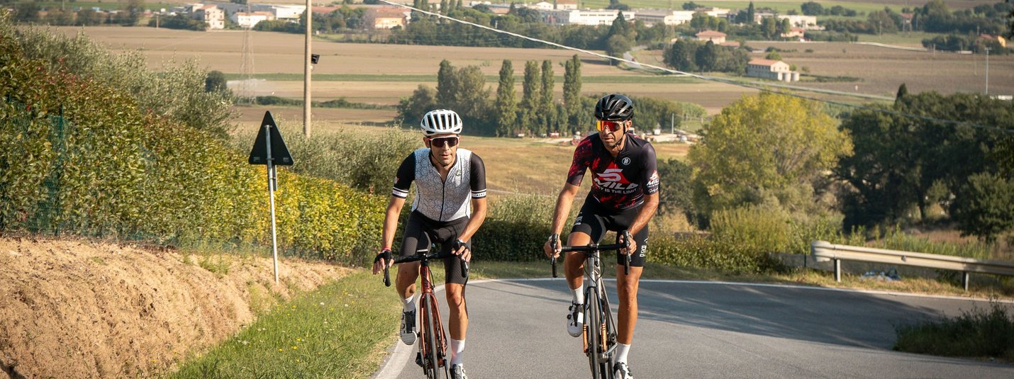 Zwei Radfahrer fahren auf einer Landstraße durch eine ländliche Gegend bei klarem Wetter