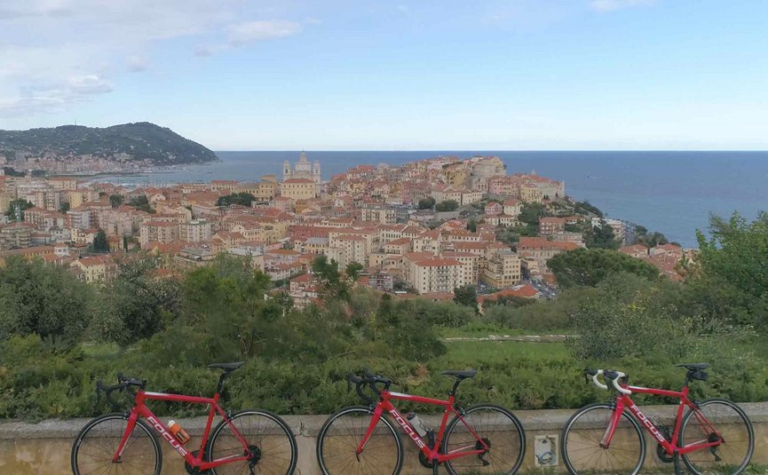 Tre biciclette da corsa rosse davanti a una città costiera sotto il cielo azzurro