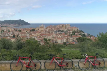 Three red road bikes overlooking a coastal town under a blue sky