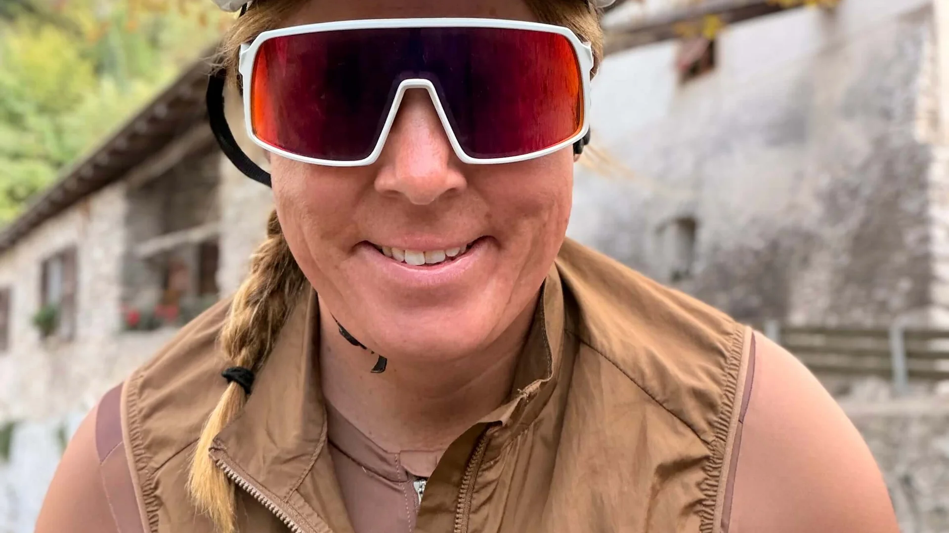 Woman wearing bike helmet and sunglasses in brown sportswear smiling