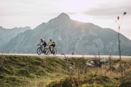 Due ciclisti su strada di montagna con alta montagna al tramonto