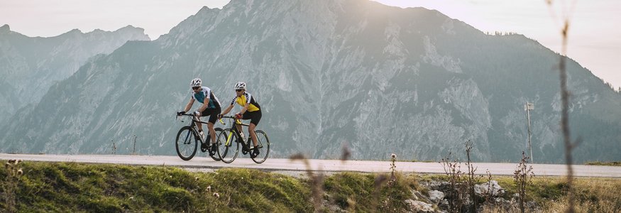 Due ciclisti su strada di montagna con alta montagna al tramonto